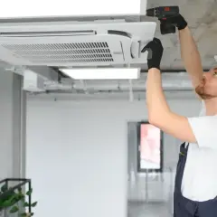 Instalator w kasku montuje klimatyzator kasetonowy na suficie.