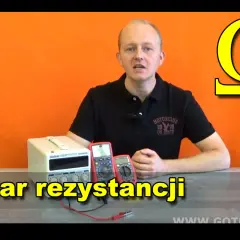 Mężczyzna przy stole z miernikami i zasilaczem, obok symbol omegi. Temat: pomiar rezystancji, czyli jednostka oporu.