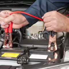 Ręce mechanika podłączają kable rozruchowe do akumulatora samochodowego, rozpoczynając czas ładowania akumulatora.
