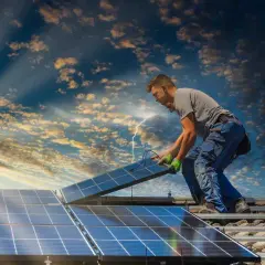 Instalator montuje panele słoneczne na dachu, przygotowując dom do systemu net metering. Słońce przebija się przez chmury.