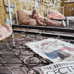 Opuszczona sala szpitalna, zniszczona lalka na łóżku, zardzewiałe sprężyny i gazeta z napisem "МЕДИЦИНСКАЯ СЕСТРА" - przejmujące świadectwo czarnobylskich skutków.
