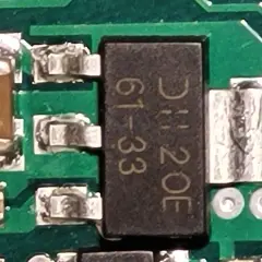 Czarny element z oznaczeniem "DH 20E 61-33" to elektroda tranzystora, otoczona innymi komponentami na zielonej płytce drukowanej.