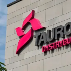 Logo Tauron Dystrybucja na szarej ścianie budynku. Zwiększenie mocy przyłączeniowej Tauron to klucz do rozwoju.