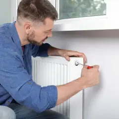 Mężczyzna używa śrubokręta, by odpowietrzyć grzejnik. To prosty sposób na pozbycie się powietrza z instalacji grzewczej.