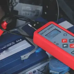Tester akumulatorów podłączony do baterii samochodowej. Pokazuje napięcie 14.25V. To prosty sposób, jak sprawdzić akumulator.
