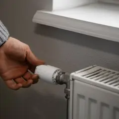 Dłoń reguluje termostat grzejnika, by zapewnić optymalną temperaturę w pomieszczeniu.