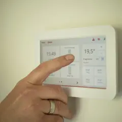 Dłoń dotyka ekranu termostatu, sprawdzając zużycie prądu. To może pomóc w osiągnięciu średniego zużycia prądu dla 2 osób.