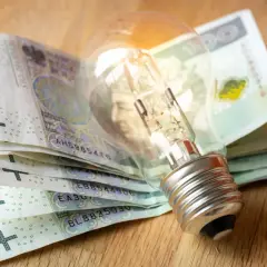 Żarówka na stosie banknotów 100 zł symbolizuje wysokie koszty energii. Dodatek energetyczny może pomóc w pokryciu rachunków.