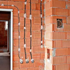 Instalacja elektryczna bezpuszkowa w budowie. Widoczne kable i otwory w ceglanych ścianach.