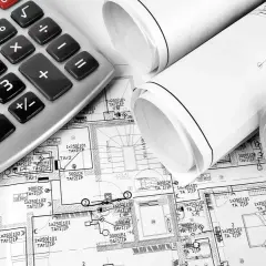 Kalkulator i zwoje planów budowlanych, sugerujące koszt instalacji elektrycznej.