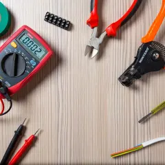 Narzędzia elektryczne: multimetr, kombinerki, ściągacz izolacji, śrubokręt, taśma izolacyjna i złączka. Widać też kabel z żyłami, w tym przewód neutralny.