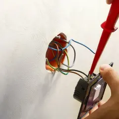 Instalator podłącza podwójny włącznik światła 2 kable, używając próbnika napięcia. Widać przewody w puszce instalacyjnej.