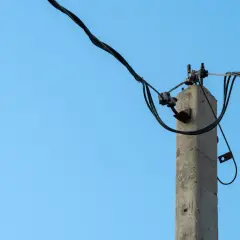 Stary, betonowy słup na działce, który stoi tam od ponad 30 lat, z plątaniną kabli na tle błękitnego nieba.