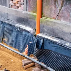 Prace przy izolacji fundamentów w starym domu. Widoczna membrana kubełkowa chroniąca ścianę przed wilgocią.