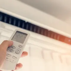Dłoń trzymająca pilot do klimatyzacji z widoczną temperaturą 22 stopnie.