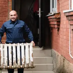 Fachowiec niesie stary grzejnik, przygotowując się do wymiany grzejnika w bloku.