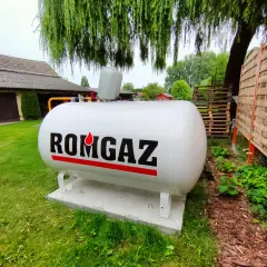 Biały zbiornik na gaz ziemny z napisem ROMGAZ, podłączony do instalacji ogrzewania gazowego z butli.