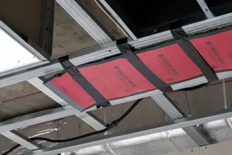 Instalacja grzejnika na podczerwień w suficie podwieszanym. Wady montażu widoczne na taśmie mocującej.
