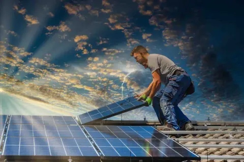 Instalator montuje panele słoneczne na dachu, przygotowując dom do systemu net metering. Słońce przebija się przez chmury.