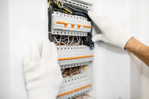 Ręce w białych rękawiczkach pracują przy rozdzielni elektrycznej z bezpiecznikami.