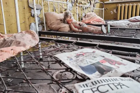 Opuszczona sala szpitalna, zniszczona lalka na łóżku, zardzewiałe sprężyny i gazeta z napisem "МЕДИЦИНСКАЯ СЕСТРА" - przejmujące świadectwo czarnobylskich skutków.