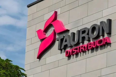 Logo Tauron Dystrybucja na szarej ścianie budynku. Zwiększenie mocy przyłączeniowej Tauron to klucz do rozwoju.