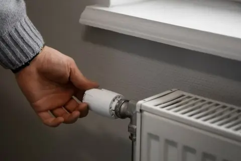 Dłoń reguluje termostat grzejnika, by zapewnić optymalną temperaturę w pomieszczeniu.