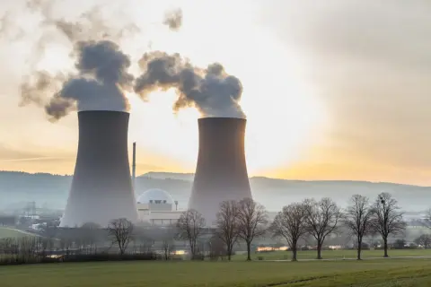 Dwie chłodnie kominowe elektrowni jądrowej z wydobywającą się parą na tle zachodzącego słońca.
