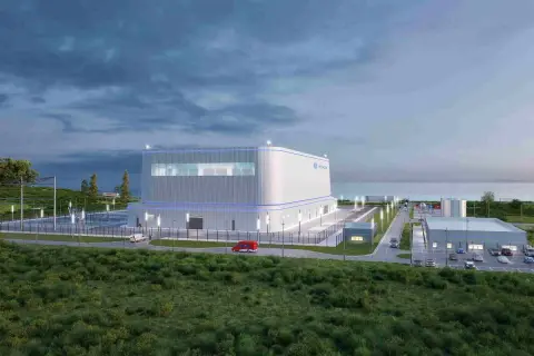 Nowoczesny reaktor jądrowy Hitachi, otoczony zielenią i infrastrukturą, z widokiem na morze.