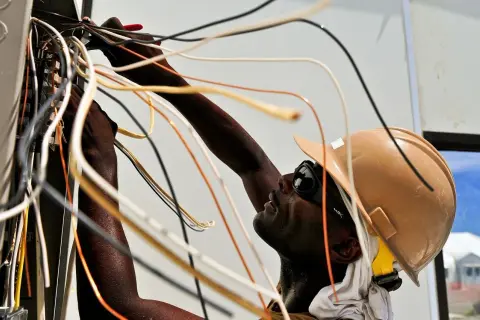 Elektryk w kasku i okularach pracuje przy instalacji elektrycznej, łącząc przewody. To dobry przykład, jak zostać elektrykiem.