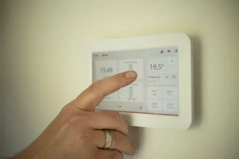 Dłoń dotyka ekranu termostatu, sprawdzając zużycie prądu. To może pomóc w osiągnięciu średniego zużycia prądu dla 2 osób.