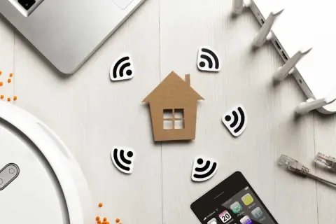 Dom z symbolami Wi-Fi, laptop, router, telefon i robot sprzątający. Wszystko to tworzy obraz inteligentnego domu, gdzie technologia i komfort idą w parze, a zasięg sieci jest wszędzie, minimalizując potencjalne **emf**.