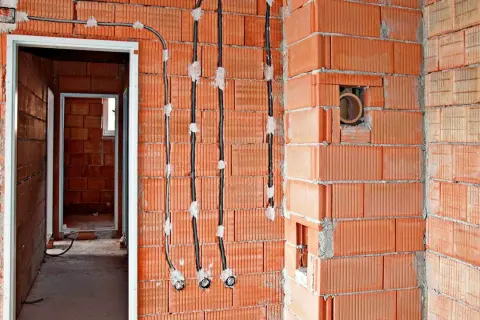 Instalacja elektryczna bezpuszkowa w budowie. Widoczne kable i otwory w ceglanych ścianach.
