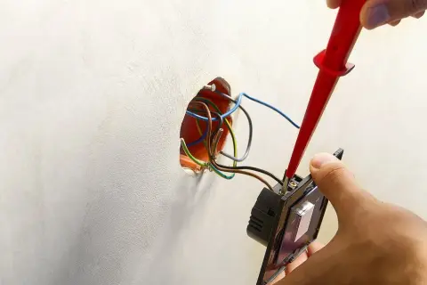 Instalator podłącza podwójny włącznik światła 2 kable, używając próbnika napięcia. Widać przewody w puszce instalacyjnej.