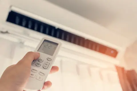 Dłoń trzymająca pilot do klimatyzacji z widoczną temperaturą 22 stopnie.