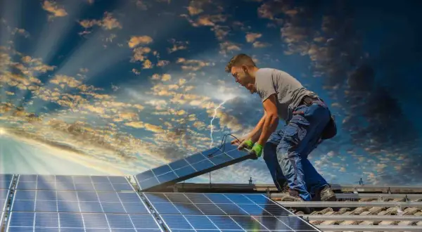 Instalator montuje panele słoneczne na dachu, przygotowując dom do systemu net metering. Słońce przebija się przez chmury.