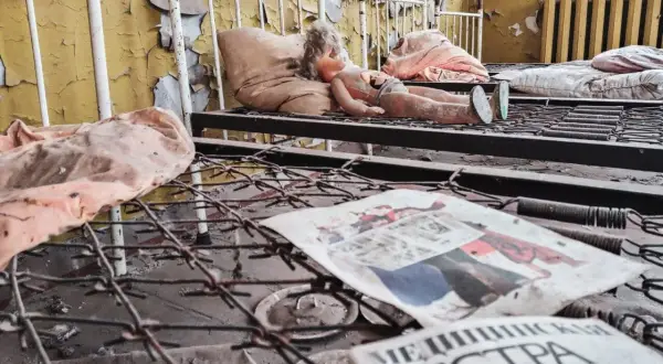 Opuszczona sala szpitalna, zniszczona lalka na łóżku, zardzewiałe sprężyny i gazeta z napisem "МЕДИЦИНСКАЯ СЕСТРА" - przejmujące świadectwo czarnobylskich skutków.