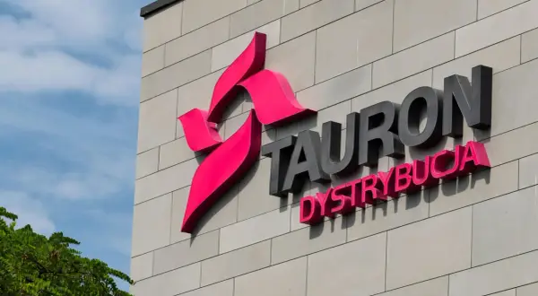 Logo Tauron Dystrybucja na szarej ścianie budynku. Zwiększenie mocy przyłączeniowej Tauron to klucz do rozwoju.