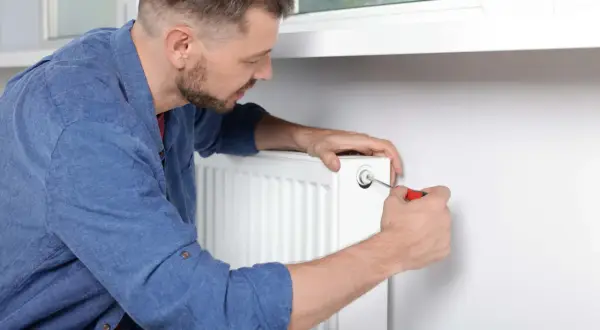 Mężczyzna używa śrubokręta, by odpowietrzyć grzejnik. To prosty sposób na pozbycie się powietrza z instalacji grzewczej.