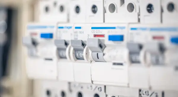 Szukasz informacji, jaki bezpiecznik do gniazdek? Na zdjęciu widać rząd białych wyłączników nadprądowych w rozdzielnicy elektrycznej, każdy z dźwignią i oznaczeniem prądowym.