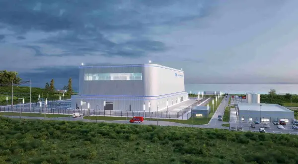 Nowoczesny reaktor jądrowy Hitachi, otoczony zielenią i infrastrukturą, z widokiem na morze.