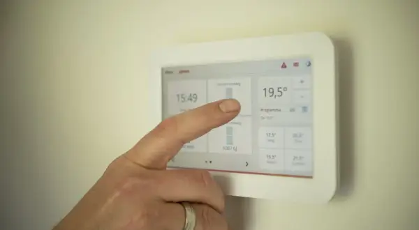 Dłoń dotyka ekranu termostatu, sprawdzając zużycie prądu. To może pomóc w osiągnięciu średniego zużycia prądu dla 2 osób.