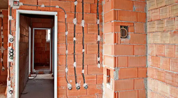 Instalacja elektryczna bezpuszkowa w budowie. Widoczne kable i otwory w ceglanych ścianach.