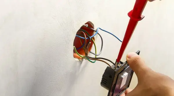 Instalator podłącza podwójny włącznik światła 2 kable, używając próbnika napięcia. Widać przewody w puszce instalacyjnej.