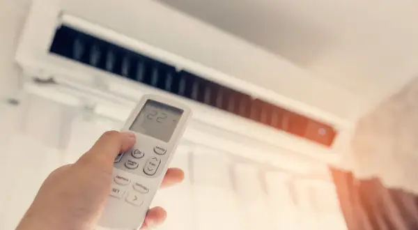 Dłoń trzymająca pilot do klimatyzacji z widoczną temperaturą 22 stopnie.
