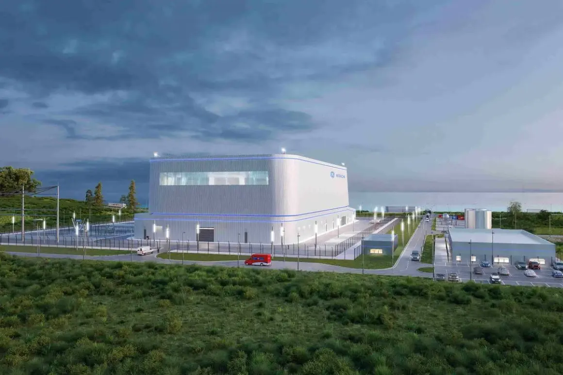 Nowoczesny reaktor jądrowy Hitachi, otoczony zielenią i infrastrukturą, z widokiem na morze.