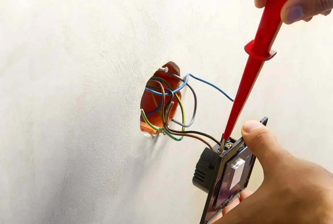 Instalator podłącza podwójny włącznik światła 2 kable, używając próbnika napięcia. Widać przewody w puszce instalacyjnej.