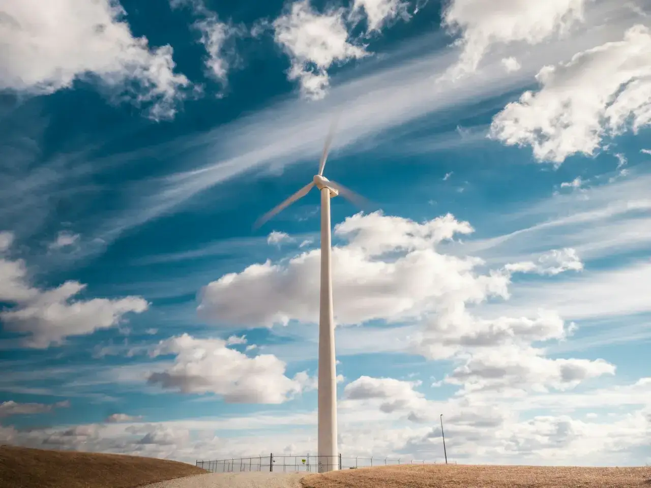 Wiatrak na tle błękitnego nieba z chmurami. To przykład OZE, czyli odnawialnych źródeł energii, które wykorzystują siłę wiatru do produkcji prądu.