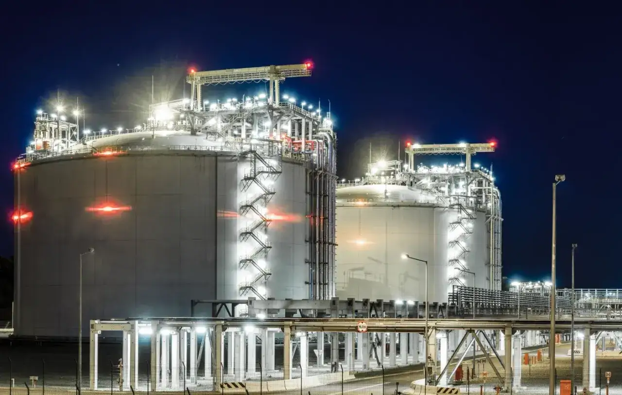 Nocny widok na gazoport z dwoma ogromnymi, oświetlonymi zbiornikami LNG.