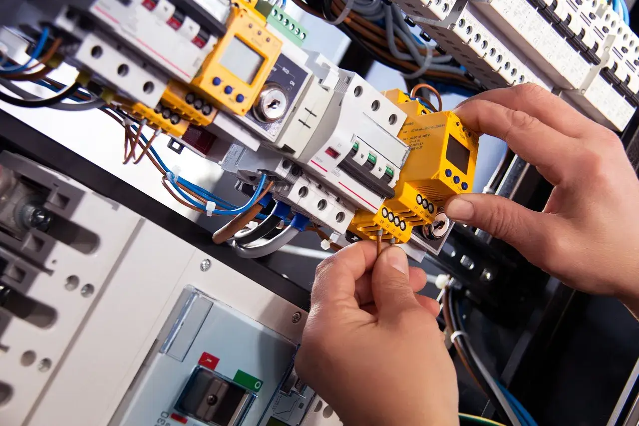 Ręce montują żółty moduł w skrzynce elektrycznej. Praktyczny element kursu elektryka od podstaw.